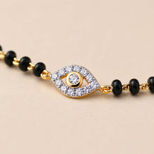 Load image into Gallery viewer, Bracelet with black beads and gold evil eye charm on a beige background
